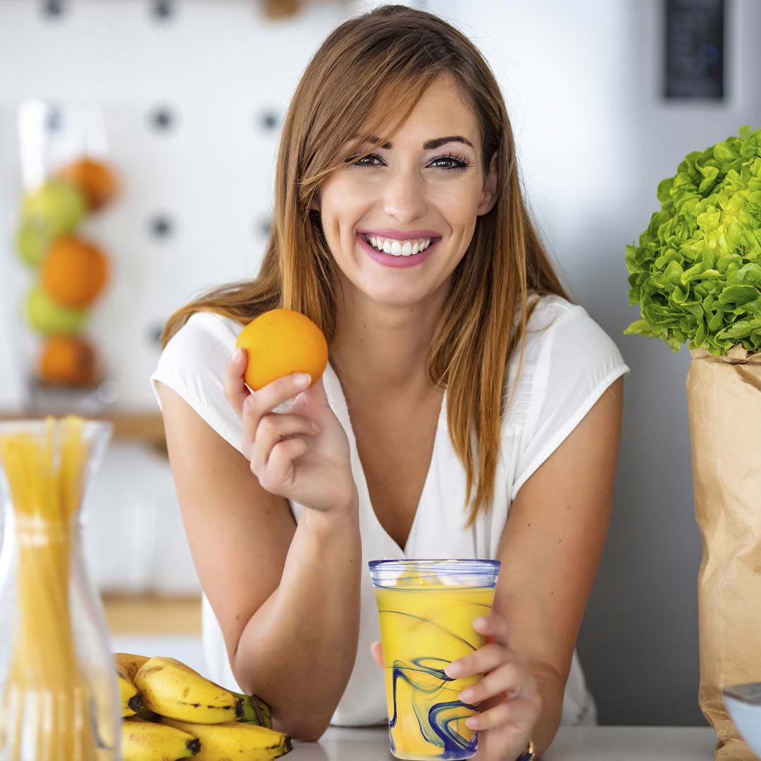 woman holding an orange and smiling while enjoying OJ from a 12.5 ounce hand blown hi-ball glass.